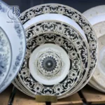 بشقاب سفید با طرح های مشکی و دور طلا روی تخته چوبی
