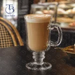 لیوان پایه دار بلور با کاپیچینو روی میز مشکی محیط کافه