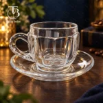فنجان نعلبکی شیشه ای از جنس بلور روی یک میز چوبی