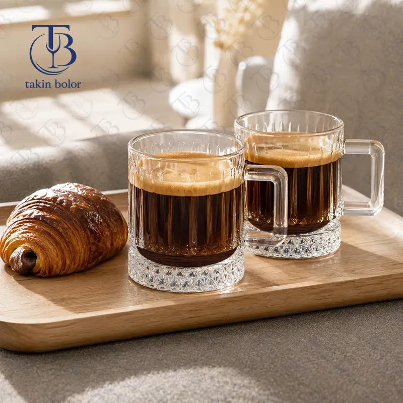 دو عدد فنجان قهوه شیشه ای از جنس بلور روی یک تخته چوب به همرا یک عدد کروسان
