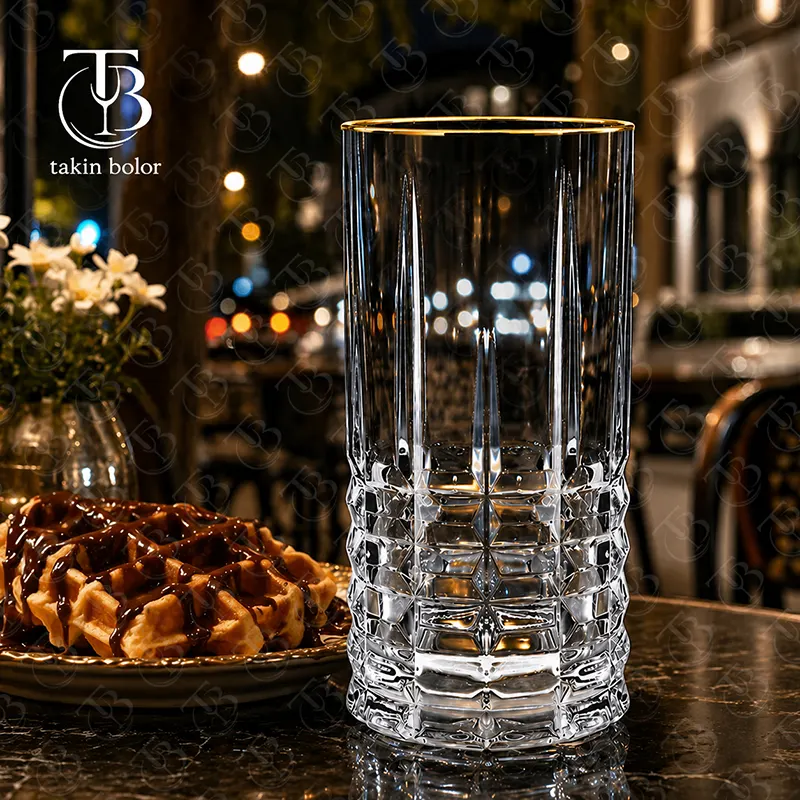 لیوان شربت خوری شیشه ای لب طلایی از جنس بلور روی یک میز