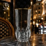 لیوان شربت خوری شیشه ای لب طلایی از جنس بلور روی یک میز