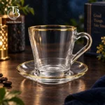 فنجان نعلبکی شیشه ای لب طلا از جنس بلور روی یک میز چوبی
